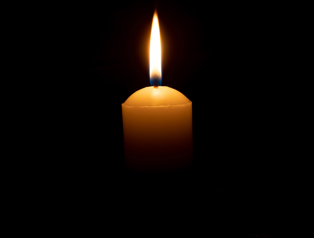 A candle in a back background perhaps signifying a digital memorial or writing and obituary.