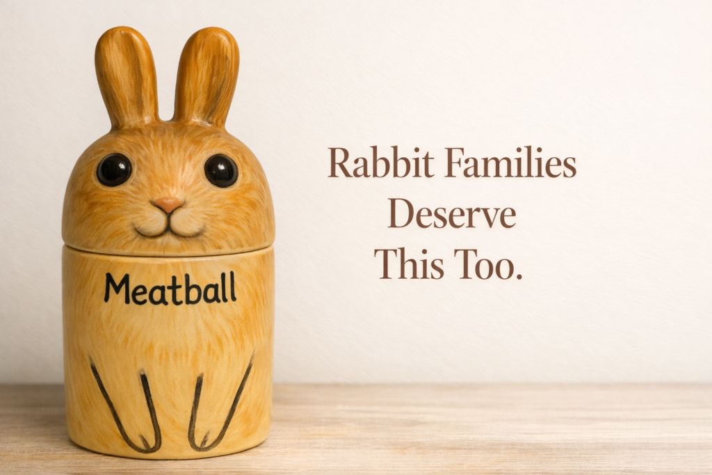 Hand-painted ceramic rabbit cremation urn with sculpted head lid and pet name lettered on golden-tan body in soft natural lighting