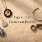 Five types of pet cremation jewelry arranged on cream linen, including a glass-infused pendant, resin paw print disc, stainless steel paw chamber pendant, locket, and cremation bracelet